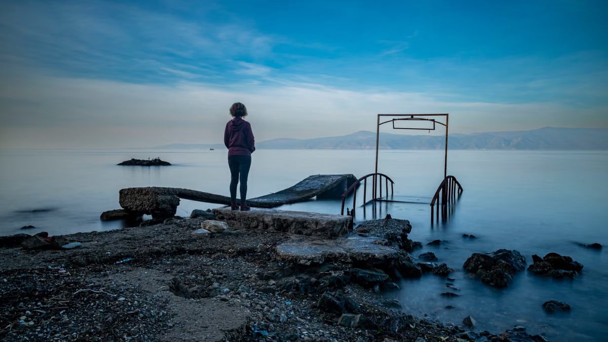 A person stands on a deserted pier overlooking a calm sea during twilight, creating a serene and contemplative mood.